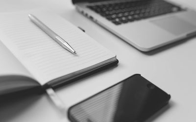 Bild eines Schreibtisches mit Notepad, Handy und Laptop